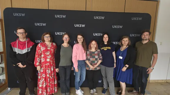 grupa 8 osób z Uczelni Łazarskiego i Uczelni Stefana Kardynała Wyszyńskiego w kampusie UKSW na tle ścianki 