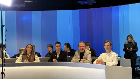 Grupa osób siedzi przy zakrzywionym pulpicie w studiu nagraniowym.