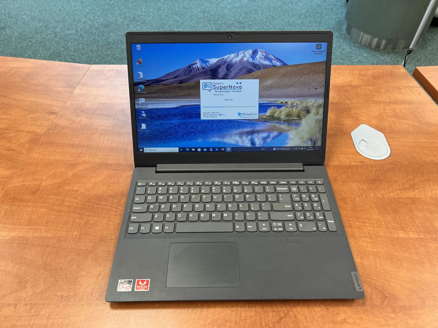 Laptop leżący na biurku. Na ekranie widoczne oprogramowanie Dolphin SuperNova, które powiększa obraz na ekranie monitora i udźwiękawia komputer.