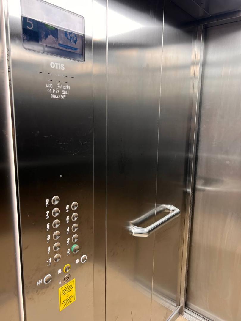 Wnętrze windy z wyświetlaczem elektronicznym, napisem „OTIS”, informacją o maksymalnym obciążeniu 1000 kg, zestawem dużych, oznakowanych alfabetem Braille'a przycisków i poręczą.