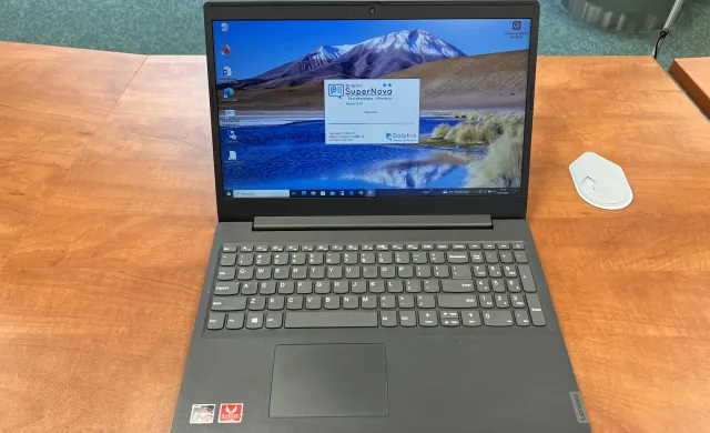 Laptop leżący na biurku. Na ekranie widoczne oprogramowanie Dolphin SuperNova, które powiększa obraz na ekranie monitora i udźwiękawia komputer.