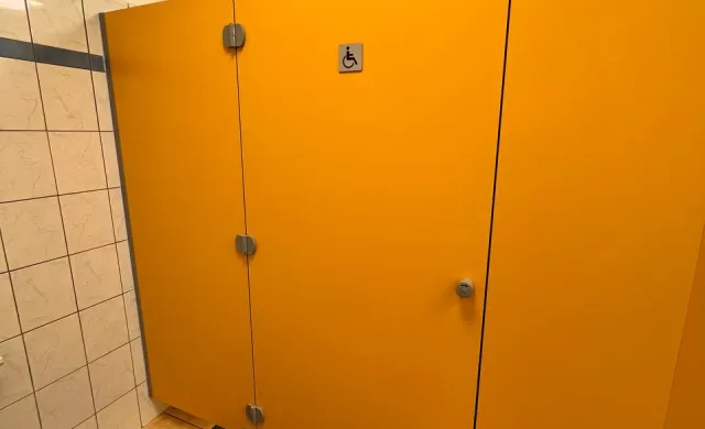 Łazienka z szeroką kabiną żółtego koloru oraz znakiem osoby na wózku inwalidzkim na szarym tle.