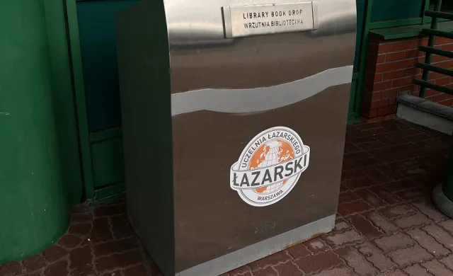 Duży metalowy kontener z logo Akademii Łazarskiego i napisami "Library Book Drop" oraz "Wrzutnia Biblioteczna".
