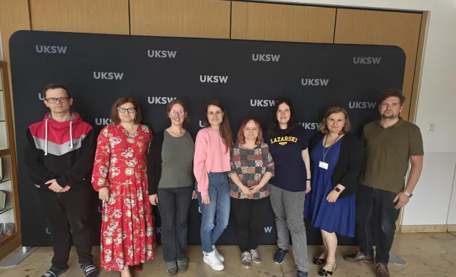 grupa 8 osób z Uczelni Łazarskiego i Uczelni Stefana Kardynała Wyszyńskiego w kampusie UKSW na tle ścianki