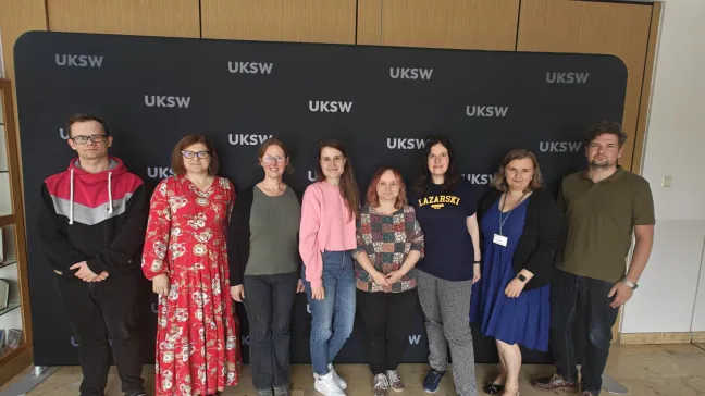 grupa 8 osób z Uczelni Łazarskiego i Uczelni Stefana Kardynała Wyszyńskiego w kampusie UKSW na tle ścianki 