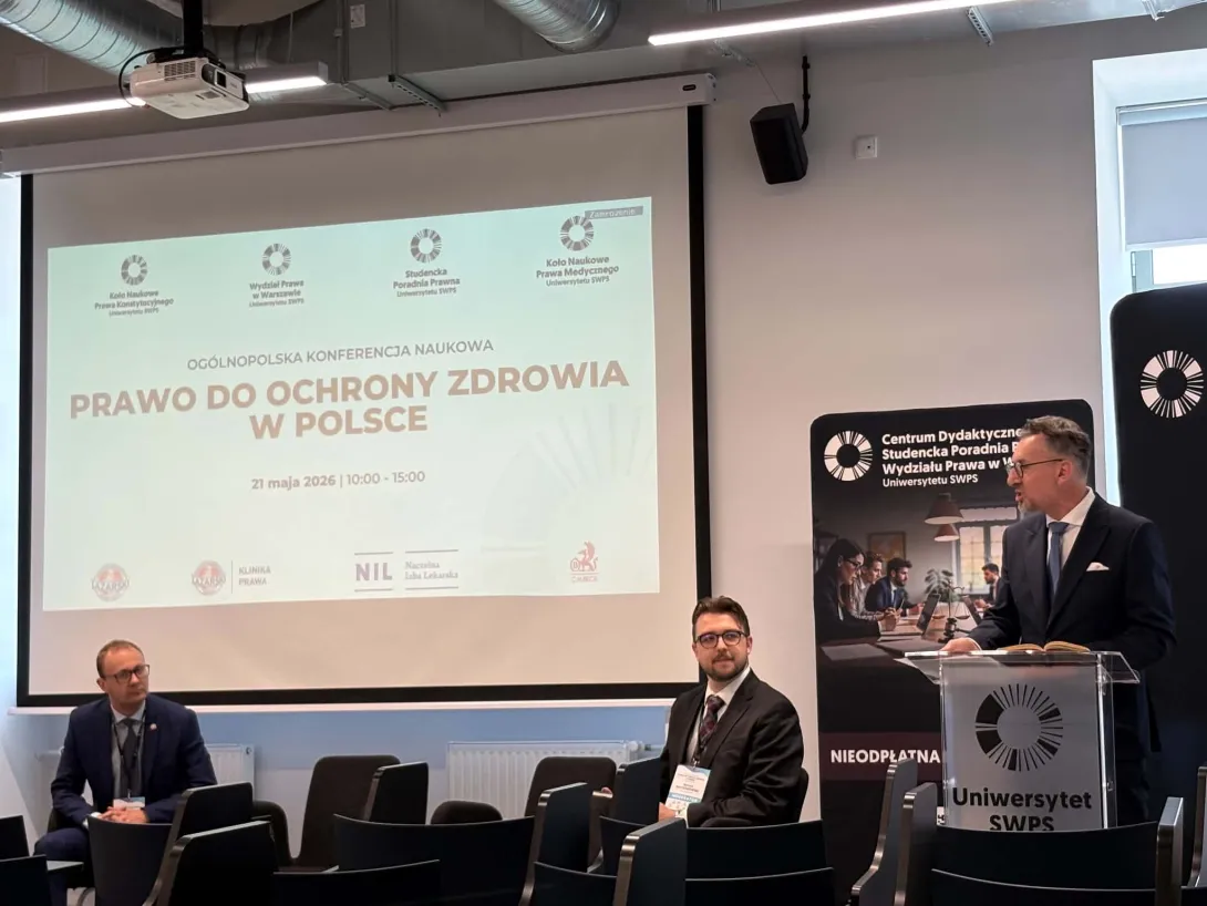 Prelegent wygłaszający przemówienie przy mównicy podczas ogólnopolskiej konferencji naukowej "Prawo do ochrony zdrowia w Polsce". W tle duży ekran z tytułem wydarzenia i logotypami współorganizatorów, w tym Uczelni Łazarskiego